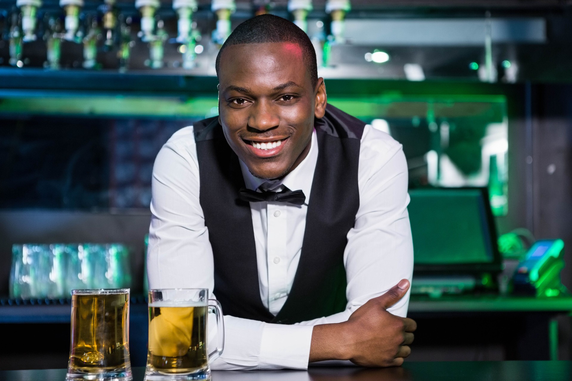Bartender leaning on bar counter with two glasses of beer in front of him